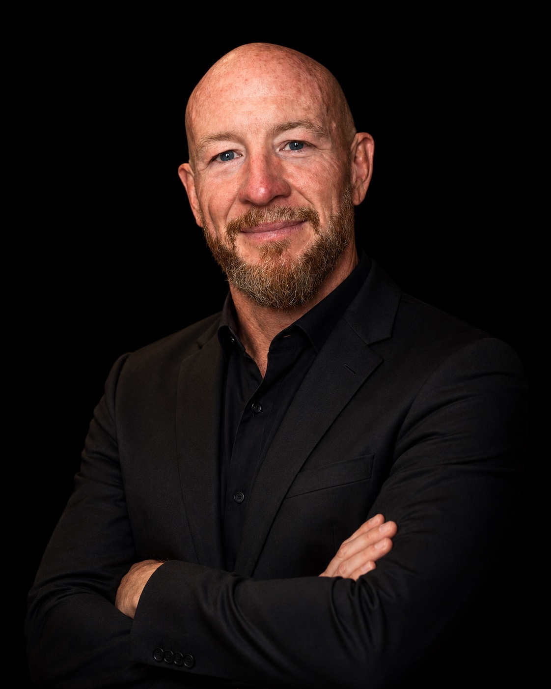 Colour portrait of Daniel Pycock wearing a black suit against a black background